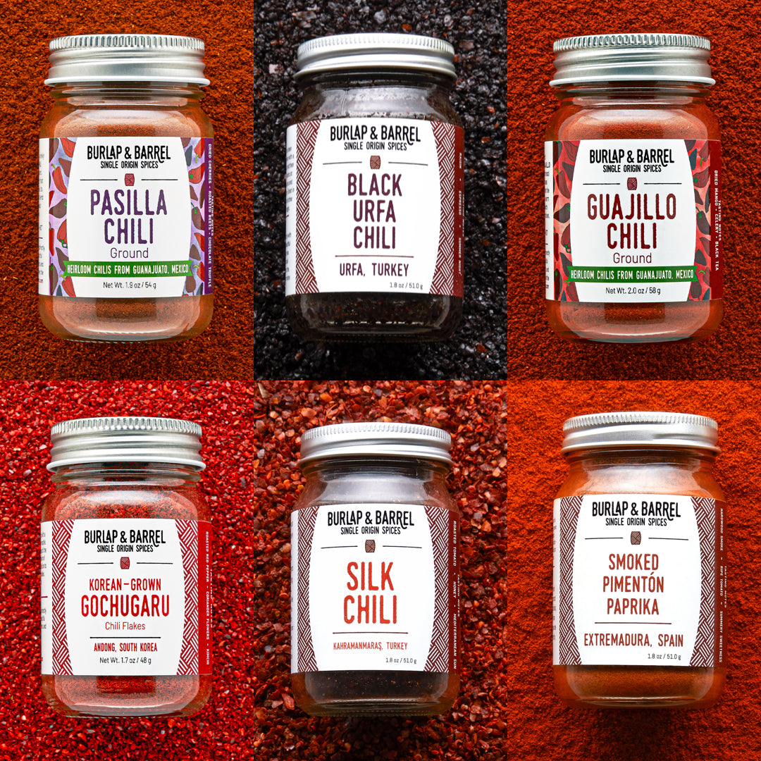 Jars of Burlap & Barrel chilis on multi-colored background of loose chili flakes