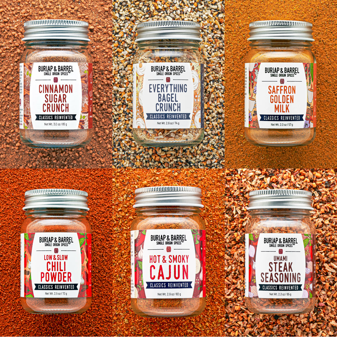 Six glass spice jars with silver lids arranged in a 2x3 grid, each set against a different spice background. The jars are labeled Burlap & Barrel, including Cinnamon Sugar Crunch, Everything Bagel Crunch, Saffron Golden Milk, Low & Slow Chili Powder, Hot & Smoky Cajun, and Umami Steak Seasoning.