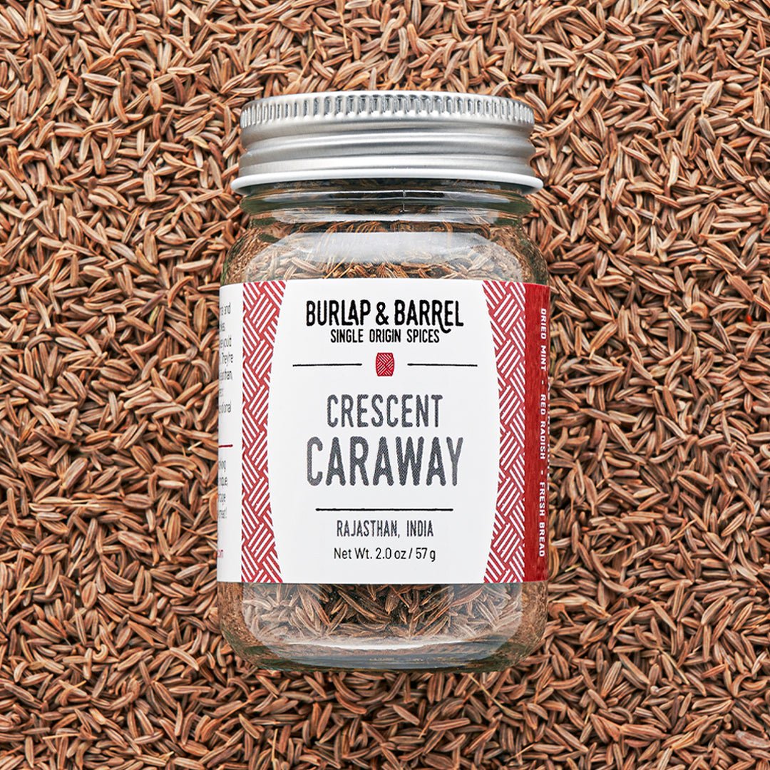 Jar of Crescent Caraway seeds with a visible label on a background of caraway seeds from Burlap & Barrel