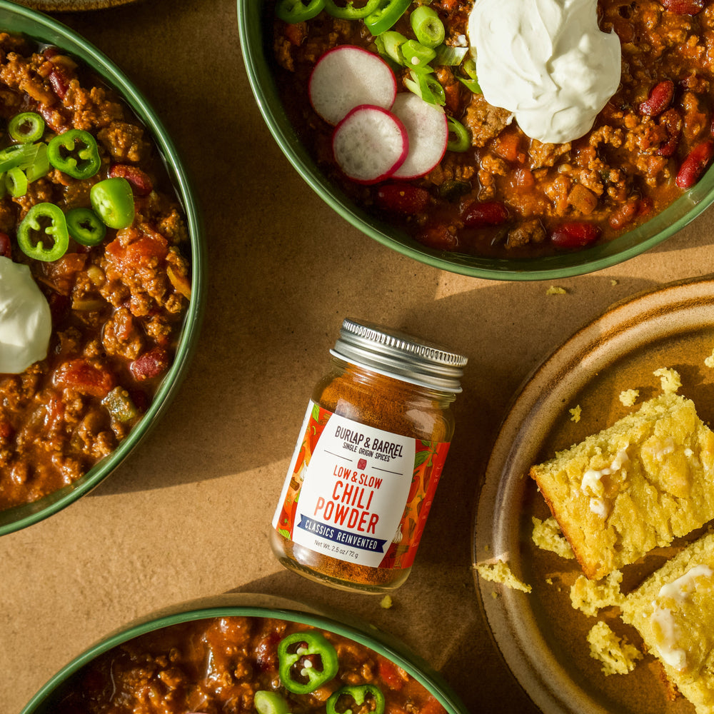 Bowls of chili with garnishes and a jar of Low & Slow Chili Powder from Burlap & Barrel