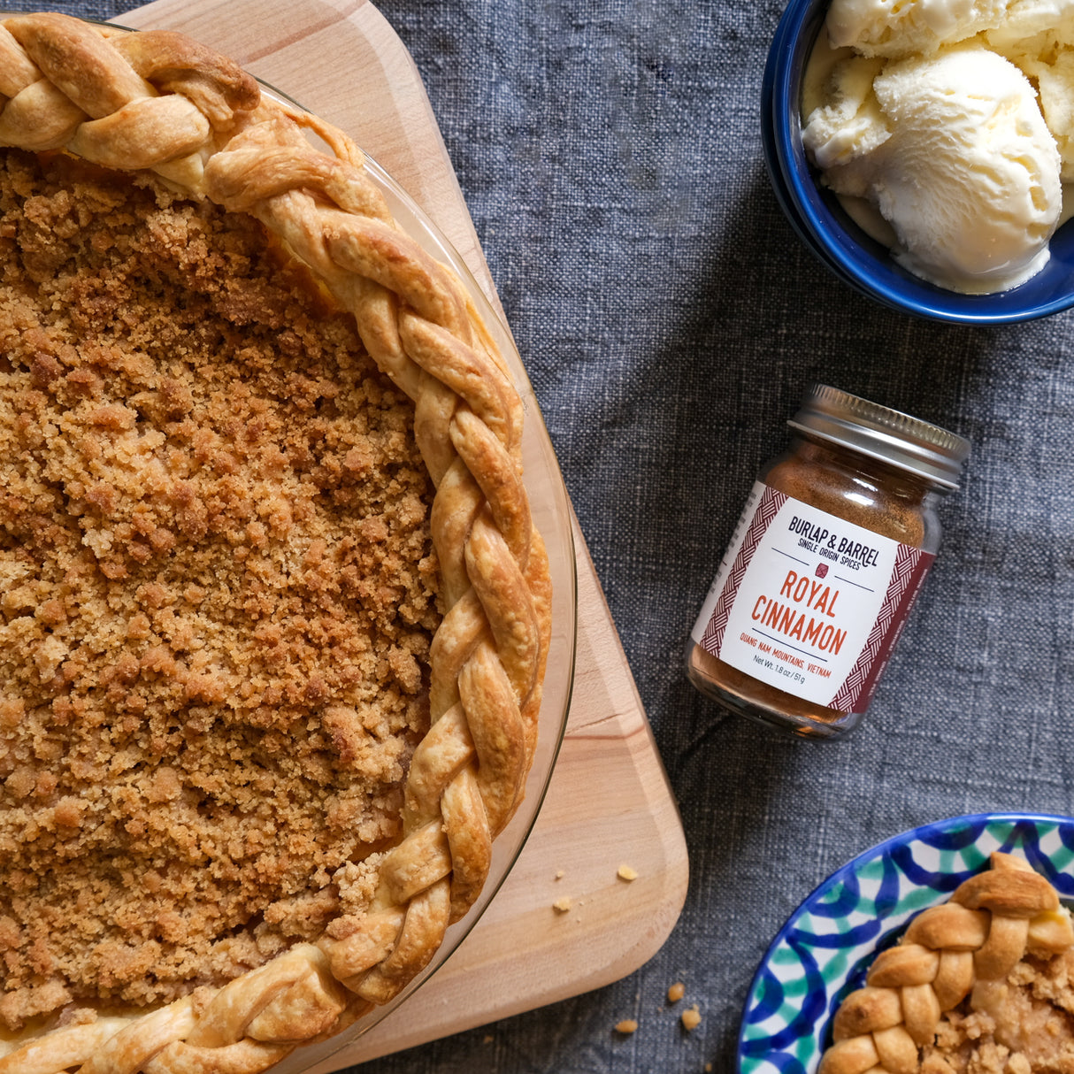 Apple pie with a braided crust on a wooden board, next to a jar of Royal Cinnamon from Burlap & Barrel