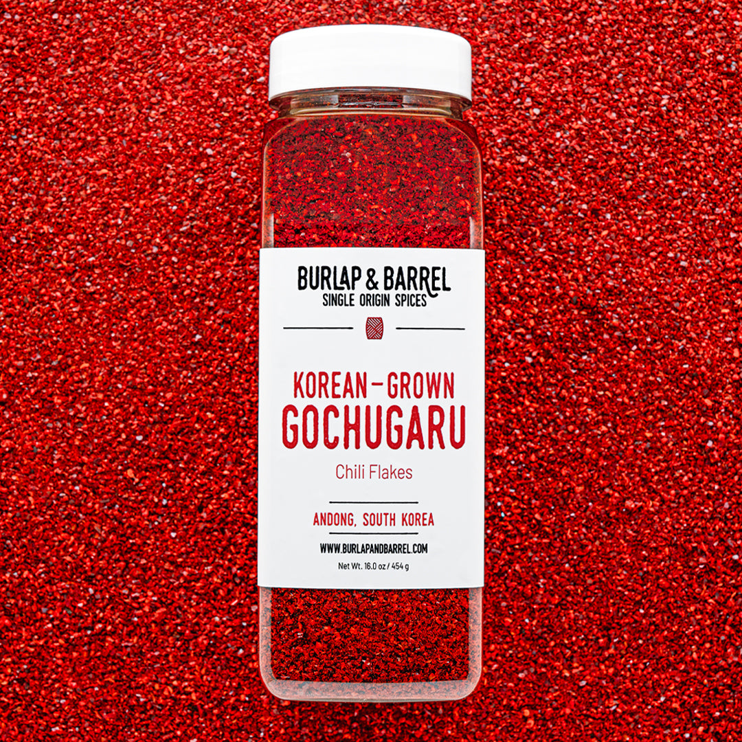 Container of Burlap & Barrel Korean-Grown Gochugaru Chili Flakes on a red background of loose chili flakes