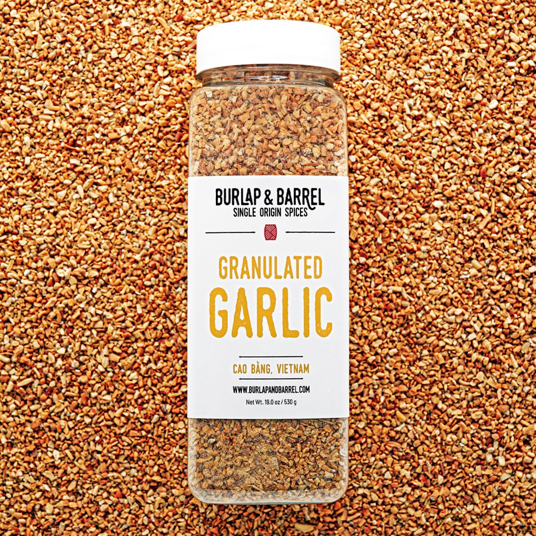Jar of granulated garlic from Burlap & Barrel on a bed of granulated garlic.