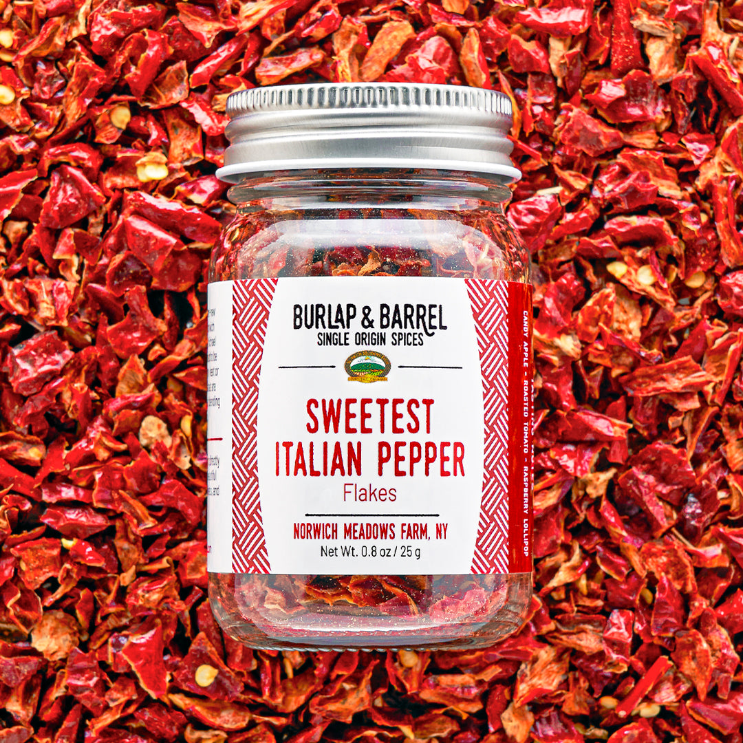 Jar of Sweetest Italian Pepper Flakes by Burlap & Barrel on a background of red pepper flakes.