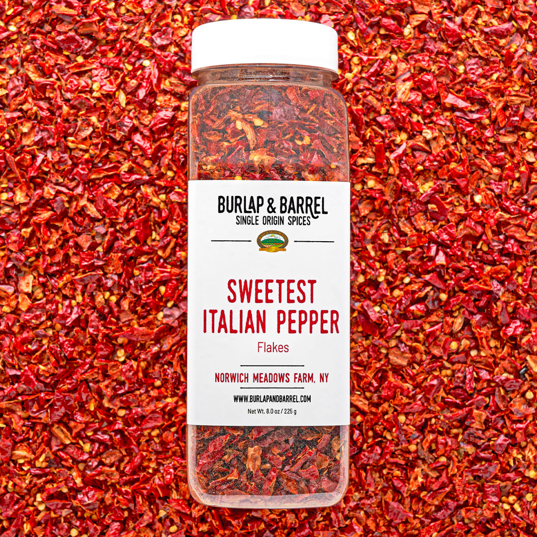 Container of Sweetest Italian Pepper Flakes by Burlap & Barrel on a background of red pepper flakes.