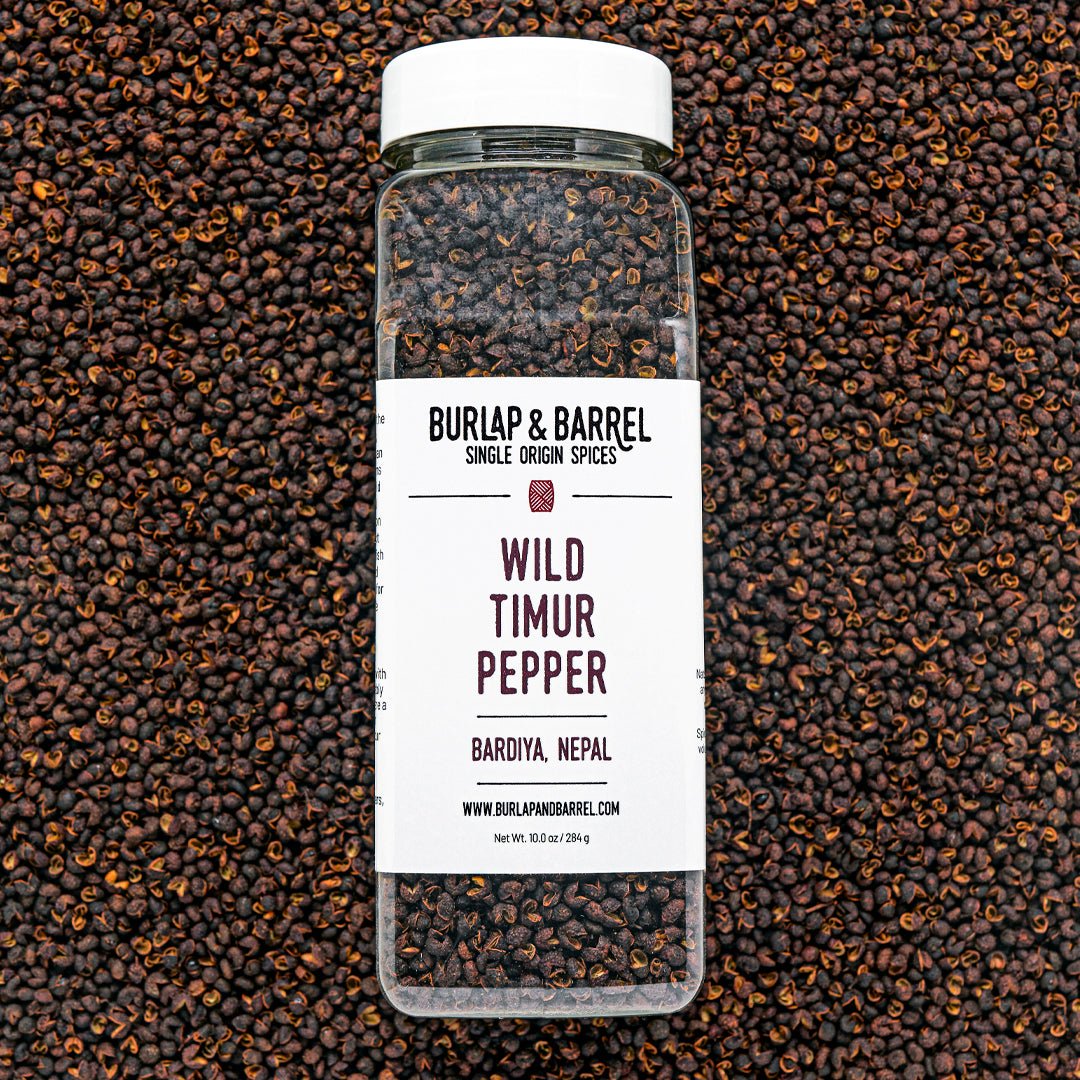 A bottle of Wild Timur Pepper by Burlap & Barrel, with the label showing the product name and origin, amidst loose peppers.