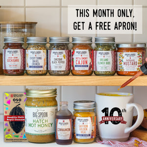 A promotional collage for Burlap & Barrel featuring multiple jars of spices and honey on wooden shelves, a box of Oso Chocolate bar, a white ceramic mug with a 10th anniversary print, and a hand holding a wooden spoon. Text at the top reads, 'THIS MONTH ONLY, GET A FREE APRON!'.
