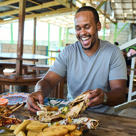 Chef Andre Fowles enjoying a meal of fish and plantains at an outdoor restaurant.