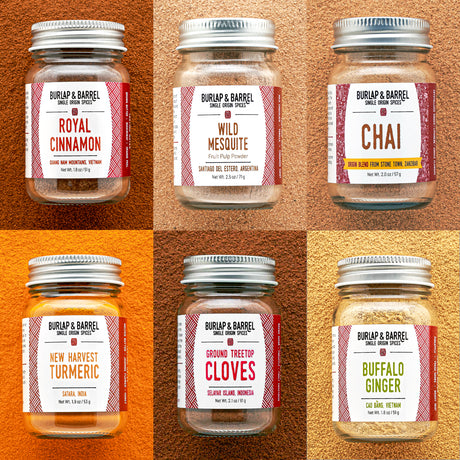 Six spice jars arranged in a 2x3 grid on a textured warm background, each with a silver metal lid and a red-and-white label. The jars are labeled Royal Cinnamon, Wild Mesquite, Chai, New Harvest Turmeric, Ground Treetop Cloves, and Buffalo Ginger.