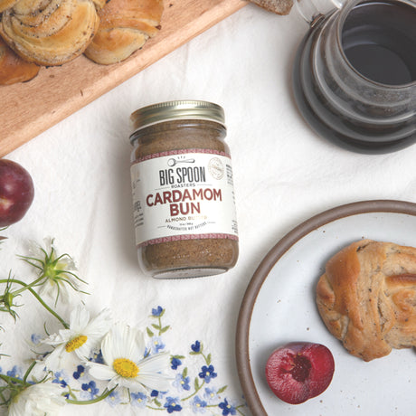 Jar of 'Big Spoon' Cardamom Bun spread on a table with pastries and flowers.