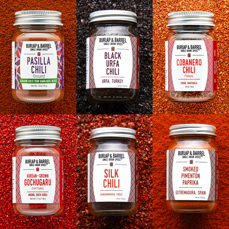Collection of Burlap & Barrel chili and spice jars on a textured red and brown background.