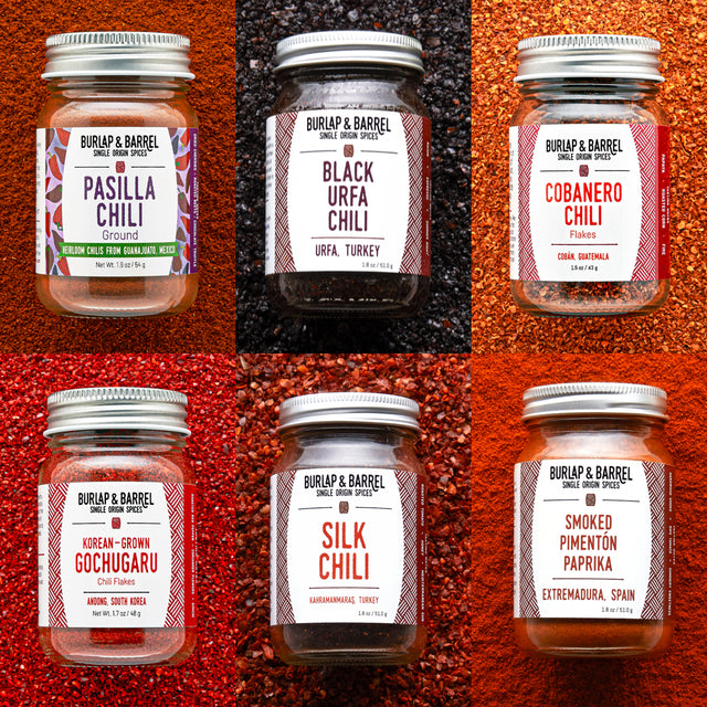 Collection of Burlap & Barrel chili and spice jars on a textured red and brown background.