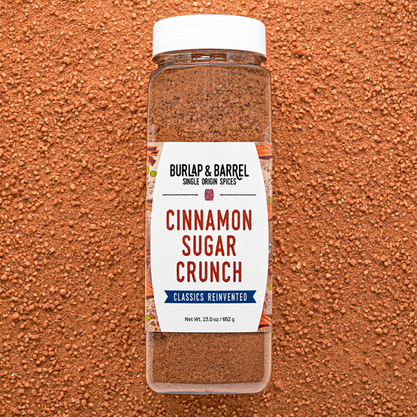 Container of BURLAP & BARREL Cinnamon Sugar Crunch spice mix on a brown textured background