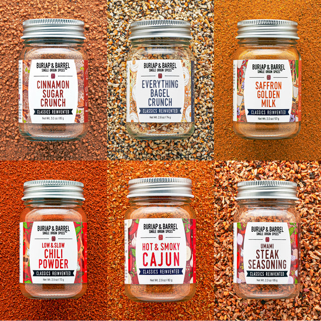 Six glass spice jars with silver lids arranged in a 2x3 grid, each set against a different spice background. The jars are labeled Burlap & Barrel, including Cinnamon Sugar Crunch, Everything Bagel Crunch, Saffron Golden Milk, Low & Slow Chili Powder, Hot & Smoky Cajun, and Umami Steak Seasoning.