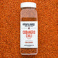 Container of cobanero chili flakes from burlap & barrel on a background of loose chili flakes.