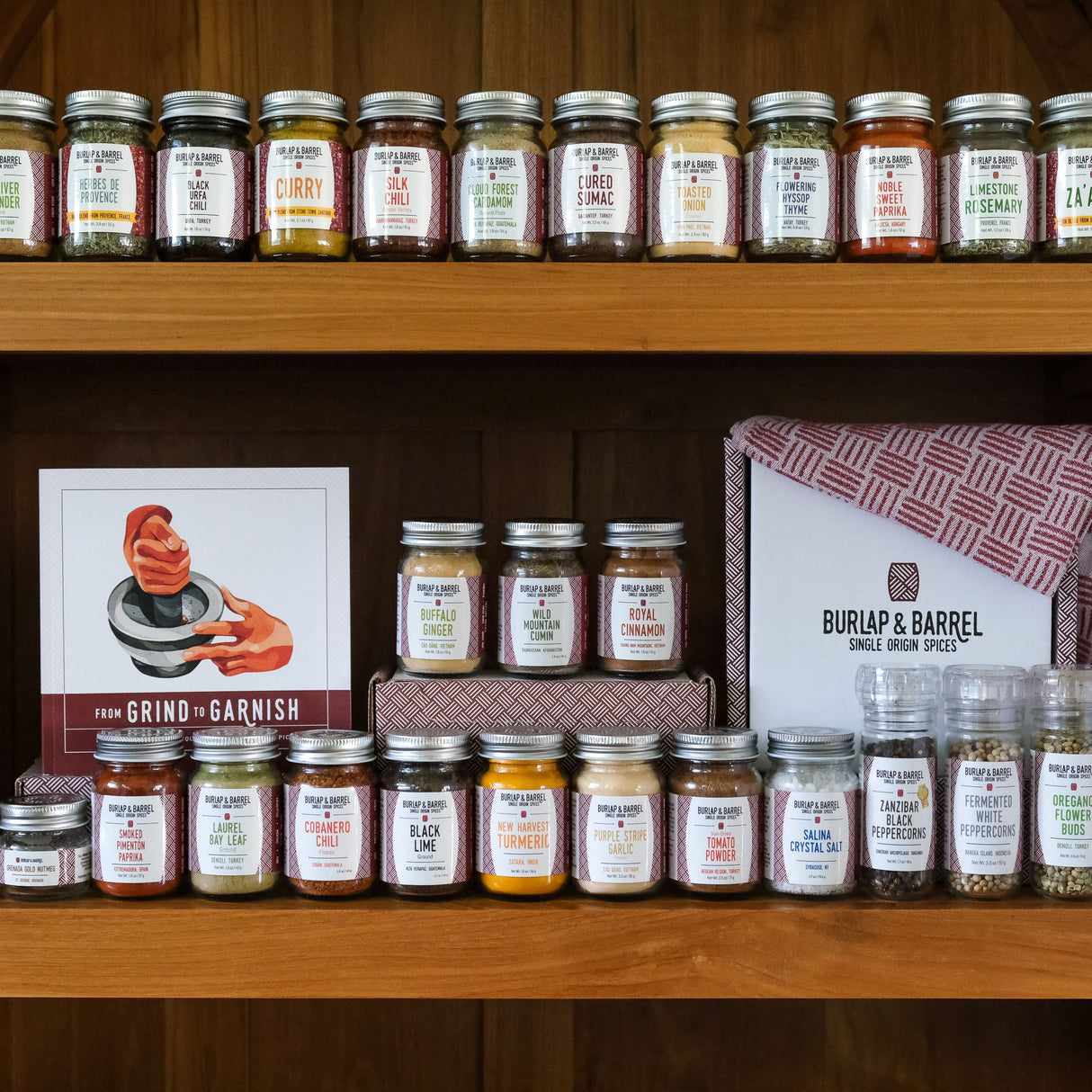 A collection of spice jars from Burlap & Barrel arranged on wooden shelves, with labels visible indicating various spice names.