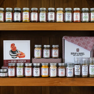 A collection of spice jars from Burlap & Barrel arranged on wooden shelves, with labels visible indicating various spice names.