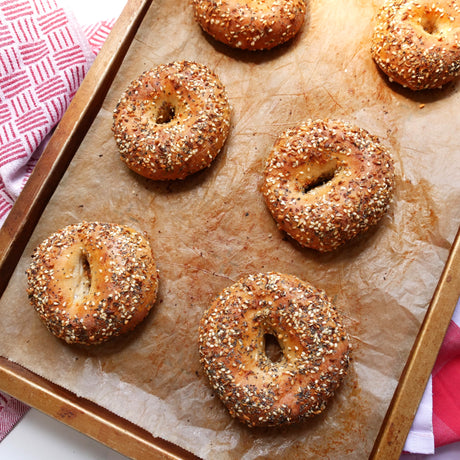 Bagels with everything bagel crunch on a baking tray lined with parchment paper.
