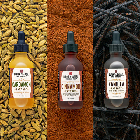 Three bottles of Burlap & Barrel spice extract syrup shown side by side: Cardamom Extract in a yellow bottle over cardamom seeds, Cinnamon Extract in a brown bottle over cinnamon powder, and Vanilla Extract in a dark bottle over vanilla beans.