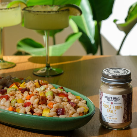 Jar of Burlap & Barrel Purple Stripe Garlic on a table with a dish of salad in the background