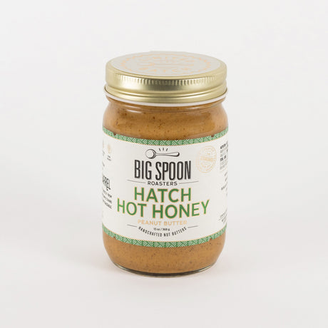 A jar of Big Spoon Roasters Hatch Hot Honey in garlic butter flavor, featuring a white label with green text and a gold metal lid, set against a plain white background.
