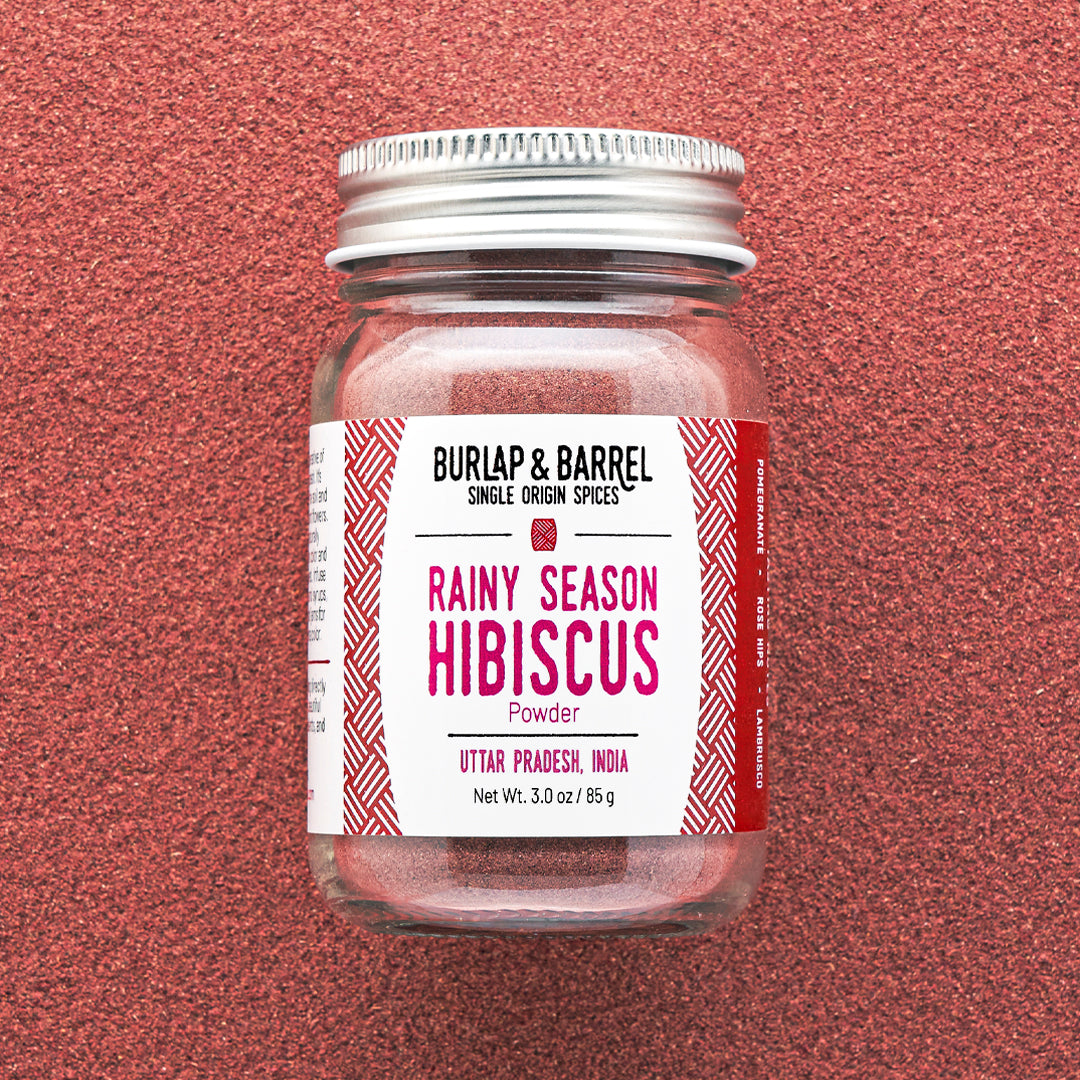 Jar of Rainy Season Hibiscus powder by Burlap & Barrel on a background of hibiscus power