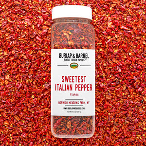 Container of Sweetest Italian Pepper Flakes by Burlap & Barrel on a background of red pepper flakes.