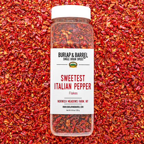 Container of Sweetest Italian Pepper Flakes by Burlap & Barrel on a background of red pepper flakes.
