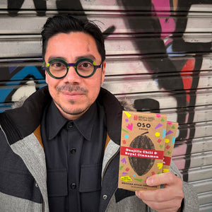 Person holding a package of Oso Gourmet coffee in front of a graffiti-covered wall.